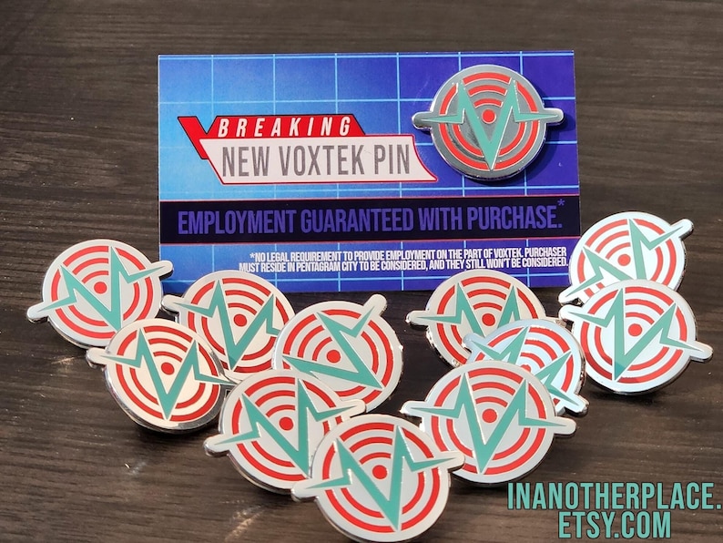 May include: A set of 10 silver-colored pins with a green and red design. The pins feature a stylized letter V with a circle around it. The text "BREAKING NEW VOXTEK PIN" and "EMPLOYMENT GUARANTEED WITH PURCHASE." is visible on a card behind the pins.