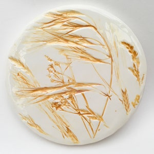May include: A white ceramic round plate with a pressed design of dried golden brown grasses and leaves.