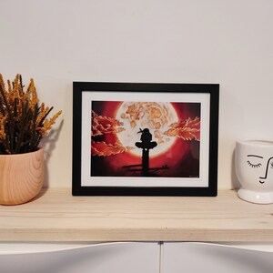 May include: A framed print of a black silhouette of a person sitting on a platform with a large red and orange moon in the background.