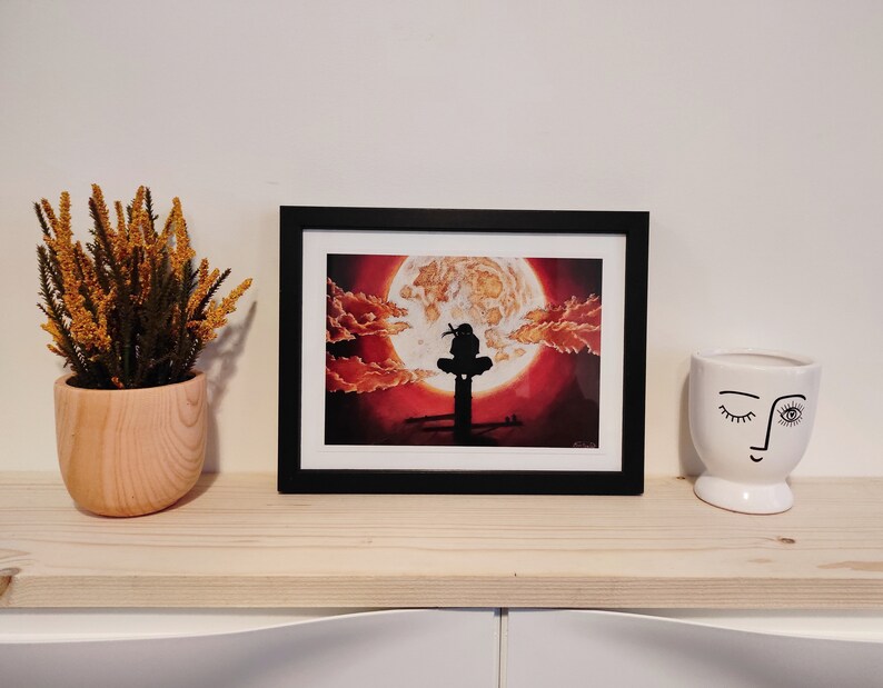 May include: A framed print of a black silhouette of a person sitting on a platform with a large red and orange moon in the background.