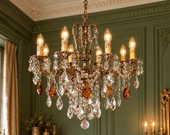 May include: An ornate brass chandelier featuring eight candle-style light bulbs, intricate metal scrollwork, and numerous hanging clear crystal prisms interspersed with several distinct amber-coloured teardrop crystals.