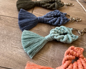 Puede incluir: Un conjunto de siete llaveros de macramé de colores con borlas. Los llaveros tienen forma de corazón y están hechos con una variedad de colores, incluyendo blanco, marrón, verde, azul, azul claro y naranja.