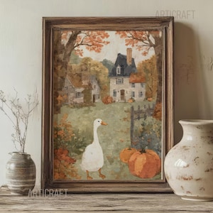 Op de afbeelding: Een ingelijste aquarel schildering toont een herfstachtige landelijke scène met een witte gans, pompoenen en een huis. Het kunstwerk staat in een bruine houten lijst en wordt tentoongesteld op een houten dressoir. Een vaas en een kleine decoratieve vaas staan op het dressoir.