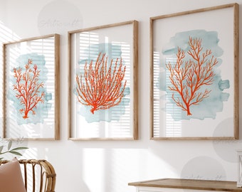 May include: Three framed coral reef art prints. Each print features a coral design in shades of orange against a light blue watercolor background. The frames are a light brown color. The prints are displayed above a white cabinet and a wicker chair.