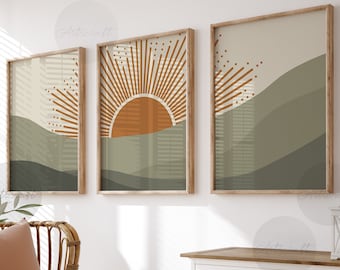 Puede incluir: Tres impresiones de arte abstracto enmarcadas con un diseño minimalista que presenta un sol y colinas en tonos marrones, naranjas y verdes. Las impresiones están colgadas en una pared blanca sobre una cómoda blanca con dos cajones.