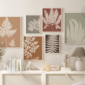 May include: A collection of six framed botanical prints featuring fern and leaf designs in shades of beige, brown, and green. The prints are displayed on a neutral-colored wall, creating a cohesive and natural aesthetic. The artwork is complemented by a lamp and decorative items.