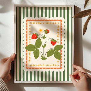 May include: A framed art print featuring a strawberry plant illustration. The artwork has a cream-colored background with a scalloped orange border. The background has green and white vertical stripes. The strawberries are red.