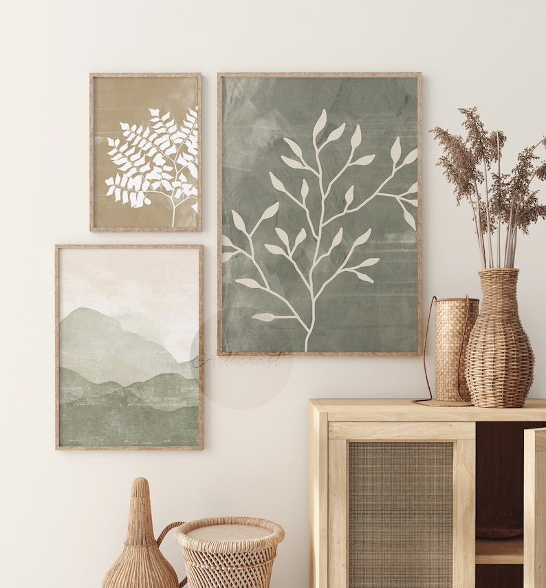 May include: Three framed prints with abstract botanical illustrations in shades of green and white. The prints are hung on a white wall above a wooden cabinet with a woven rattan door.