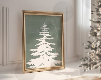 May include: A framed print with a white fir tree design on a muted green backdrop. The artwork is presented in a gold-coloured frame, positioned against a white wall. A Christmas tree with decorations is in the background, indicating a festive theme.