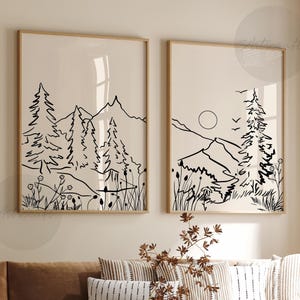 May include: Two black and white line art prints of a mountain landscape with trees and a sun. The prints are framed in natural wood frames and are hanging on a beige wall.