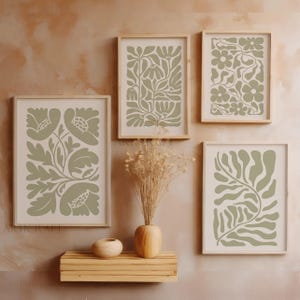 May include: Four framed botanical art prints with a neutral color palette. Each print features a different floral or leaf design in shades of green on a cream background. The frames are light wood, and the arrangement includes a vase with dried flowers.