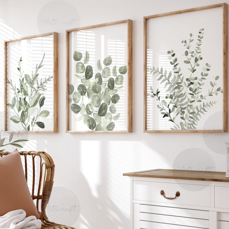 Puede incluir: Tres l&aacute;minas bot&aacute;nicas enmarcadas con ilustraciones en acuarela de hojas y follaje verdes. Las l&aacute;minas tienen marcos de madera marr&oacute;n claro y se exhiben contra una pared blanca. La obra de arte incluye eucalipto, helechos y otra vegetaci&oacute;n.