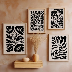 May include: Five framed art prints featuring black floral designs on a cream background. The prints are in light wood frames and are displayed on a wall. A wooden shelf holds a vase with dried flowers and a small wooden bowl.