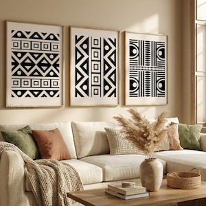 May include: Three framed wall art prints featuring black geometric patterns on a white background. The designs include repeating triangles, squares, circles, and vertical lines. The prints are displayed in light wood frames on a beige wall.