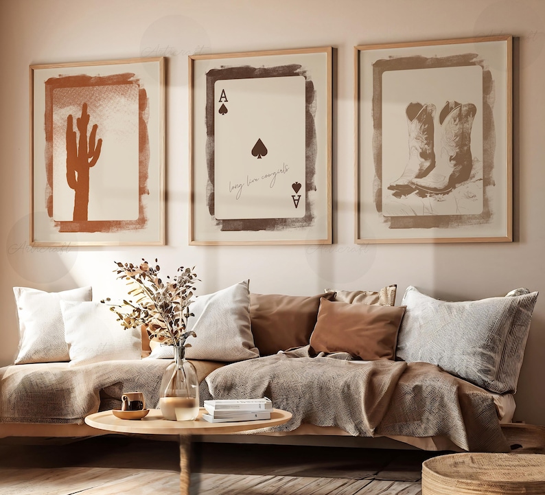 May include: Three framed prints with a desert theme. The left print features a brown silhouette of a cactus on a tan background. The center print features a brown ace of spades with the text "long live congrats" on a tan background. The right print features a pair of brown cowboy boots on a tan background.
