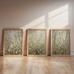 Könnte beinhalten: Drei gerahmte Kunstdrucke mit Blumenmotiven. Jeder Druck zeigt eine weiche, gedämpfte Farbpalette mit weißen und braunen Wildblumen. Die Rahmen sind aus hellfarbigem Holz gefertigt. Das Kunstwerk wird an einer hellfarbigen Wand und einem Holzboden ausgestellt.