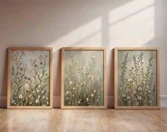 May include: Three framed floral art prints. Each print features a soft, muted color palette with white and brown wildflowers. The frames are made of light-colored wood. The artwork is displayed on a light-colored wall and wooden floor.