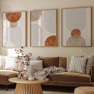 May include: Three framed abstract art prints. Each print features a beige background with geometric shapes: a semi-circle, a circle, and a series of vertical lines forming an arch. The color palette includes shades of brown, beige, and black.