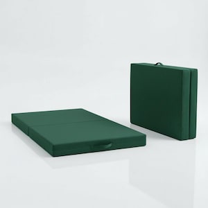 May include: A dark green folding mattress, partially unfolded, with a handle on the side. Another folded mattress stands upright, also dark green, with a handle. Both are on a white surface.