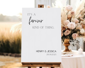 May include: White wedding sign with black text that reads "It's a forever kind of thing. Henry & Jessica 28.08.2025" on an easel in front of a rustic wooden building.
