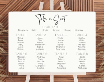 May include: White seating chart with black text for a wedding reception. The chart is titled "Take a Seat" and lists the names of guests assigned to each table. The head table includes the bride and groom's names.