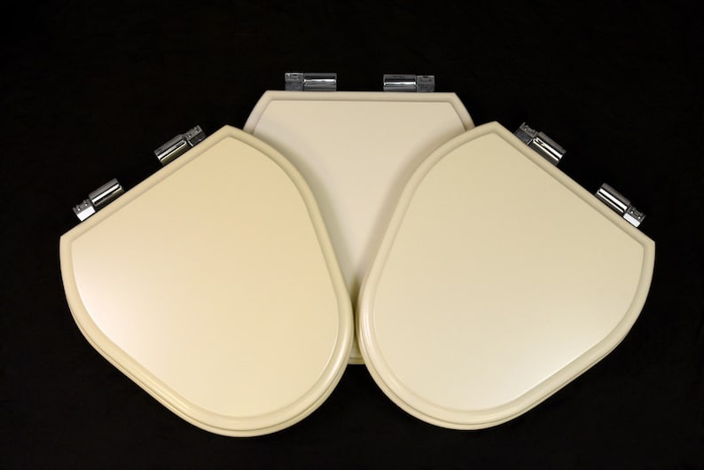 Puede incluir: Tres asientos de inodoro de color blanco roto con bisagras cromadas. Los asientos est&aacute;n dispuestos en forma triangular.