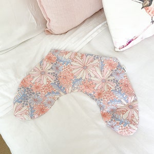 May include: A pink and blue floral patterned pregnancy pillow. The pillow is shaped like a horseshoe and is lying on a white bedspread.