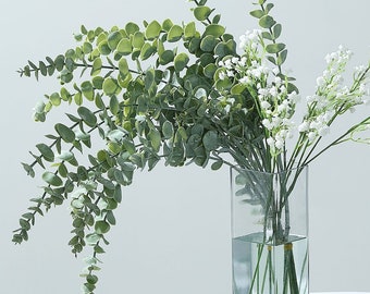 May include: A clear glass vase filled with a bouquet of white baby's breath and green eucalyptus sprigs.