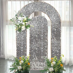 May include: A silver sequin archway with a rectangular base and an arched top, decorated with white and yellow flowers. The backdrop is suitable for weddings, parties, or photo shoots. The frame is made of wood.