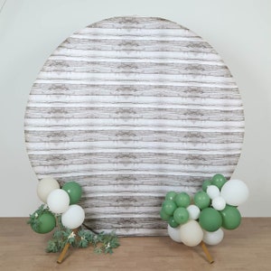 May include: A round, white wood-grain backdrop with green and white balloons on either side. The backdrop is perfect for a party or photo shoot.