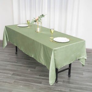 May include: A sage green satin tablecloth draped over a table with a floral centerpiece and two place settings. The tablecloth is smooth and wrinkle-free.