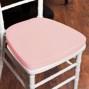 May include: A white wooden chair with a light pink cushion. The cushion is square with rounded edges and appears to be made of a smooth material. The chair has a bamboo-style design.