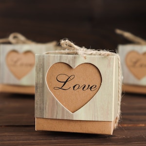 May include: A set of three small, square gift boxes with a rustic woodgrain design. Each box has a heart-shaped cutout with the word "Love" written inside. The boxes are tied with twine.