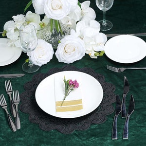 Puede incluir: Un plato de servicio de encaje negro con un plato de cena blanco en la parte superior. Una servilleta blanca con una flor rosa se coloca en el plato. El plato de servicio est&aacute; sobre un mantel verde.