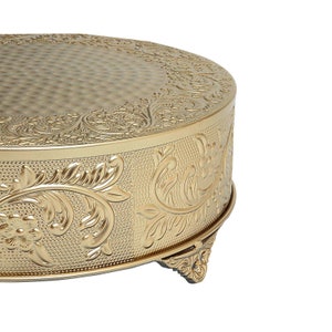 May include: Gold cake stand with an ornate floral design and three legs. The stand is made of metal and has a smooth, shiny finish.