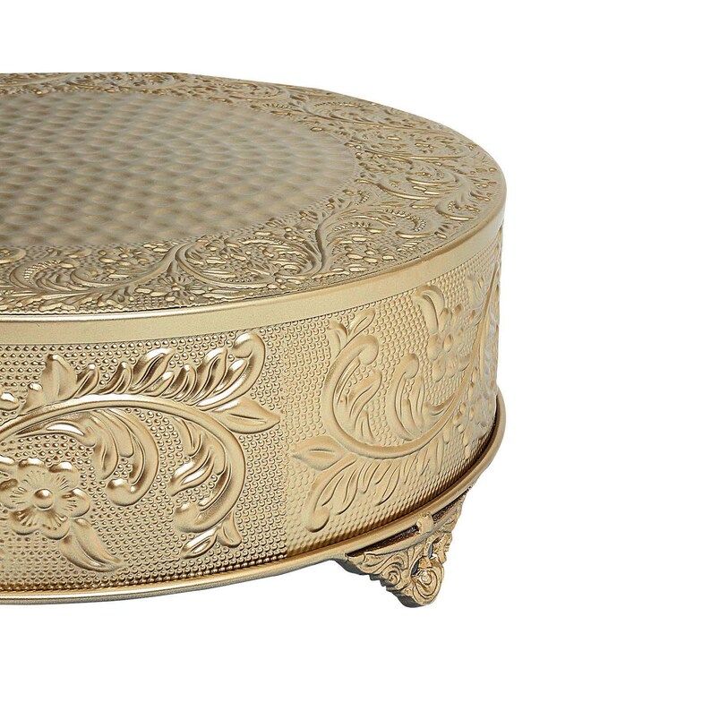 May include: Gold cake stand with an ornate floral design and three legs. The stand is made of metal and has a smooth, shiny finish.