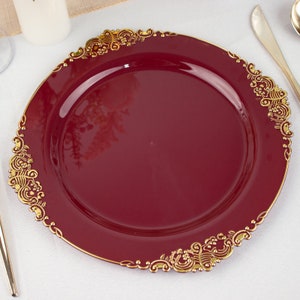 May include: A burgundy charger plate with a gold decorative rim. The rim features a delicate floral design.
