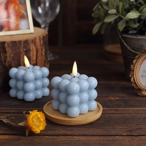May include: Two light blue bubble candles with a warm glow. The candles are on a wooden coaster and a wooden surface.