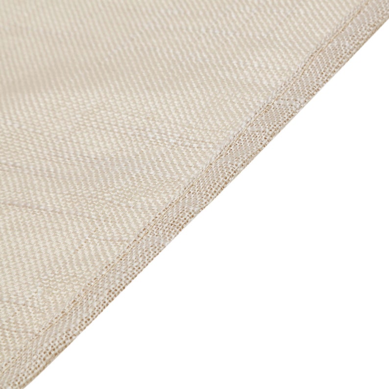 May include: Close-up of a beige fabric with a textured weave. The fabric has a subtle sheen and a delicate, stitched edge.