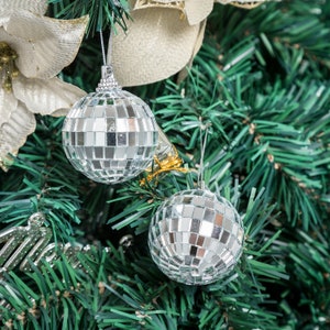 May include: Two silver disco ball ornaments hanging on a green artificial Christmas tree.