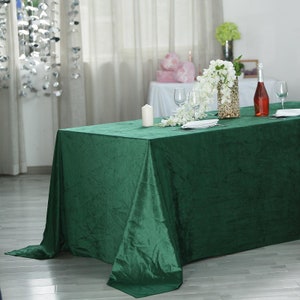 May include: A dark green velvet tablecloth draped over a table with white flowers, a candle, and wine glasses. The tablecloth is 108 inches long and 54 inches wide.