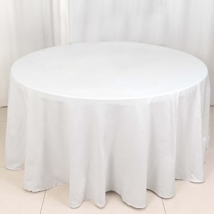 May include: A round, white tablecloth covers a table. The fabric drapes to the floor, creating soft folds. The table is set on a tiled floor, with a white curtain in the background. The tablecloth is suitable for events.