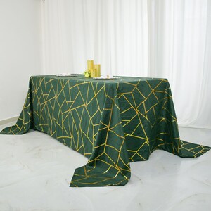 May include: A green tablecloth with a gold geometric pattern. The tablecloth is draped over a table and has a slight sheen.