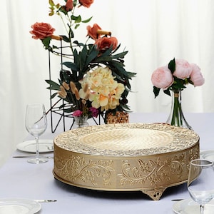 May include: Gold metal cake stand with an ornate design. The stand has a round top and three legs.