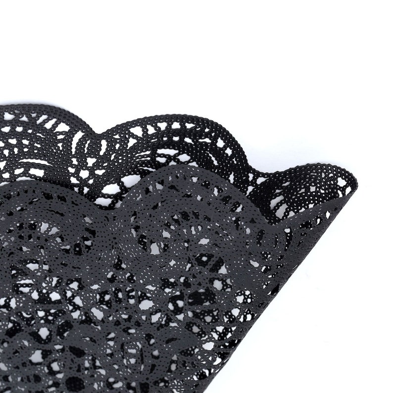 Puede incluir: Doily de encaje negro con borde festoneado. El doily est&aacute; hecho de un patr&oacute;n delicado e intrincado.