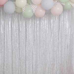 May include: A silver sequin backdrop with a garland of pastel colored balloons. The balloons are in various shades of pink, blue, green, and white.