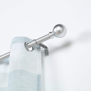 May include: Silver curtain rod with a round finial. The rod is mounted to a white wall and has a sheer white and blue curtain hanging from it.