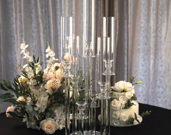 May include: A crystal candle holder with multiple tiers and a mirrored base. The holder is made of clear glass and has a modern design. It is perfect for displaying candles or other decorative items.