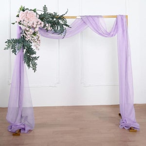 May include: A gold metal archway decorated with a lavender sheer fabric backdrop and a floral arrangement of pink roses and green leaves.