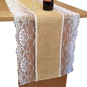 May include: A burlap table runner with white lace trim. The runner is on a wooden table and has a wine bottle and glass on top of it.